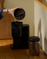 Adding coffee beans to a Fellow Opus 2 grinder in a home coffee setup
